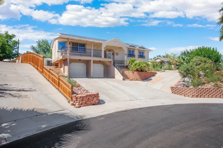 Stucco exterior with a two-car garage, concrete driveway, stone retaining walls, and a wooden fence