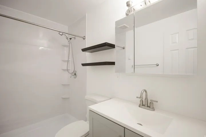 White shower surround with built-in shelving, chrome showerhead, and shower rod