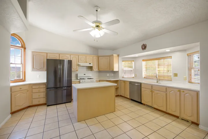 Kitchen featuring a functional island, light wood-finish cabinetry, tile flooring, stainless steel refrigerator, and a vaulted ceiling with a fan