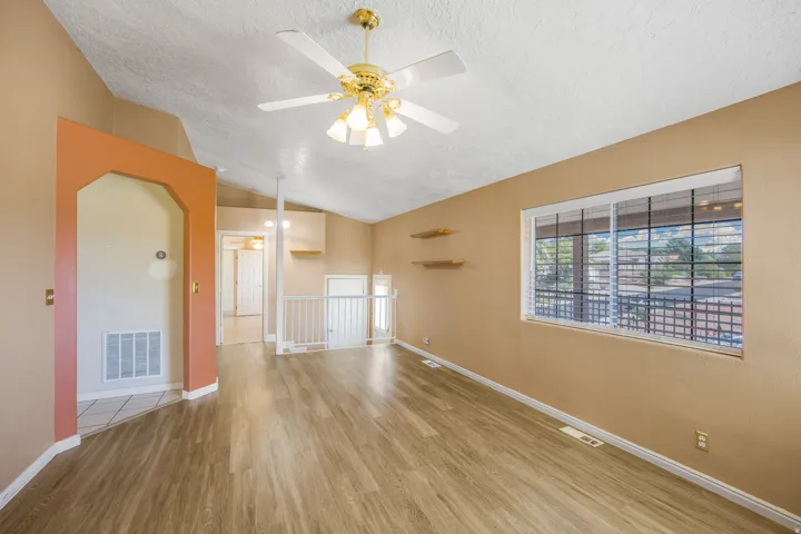 Vaulted ceiling with ceiling fan, wood-finish flooring, accent wall archway, built-in shelving, and window with blinds