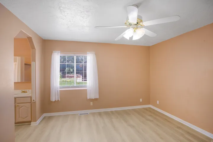 Wood-finish flooring, ceiling fan, natural light from a window, and an arched entryway