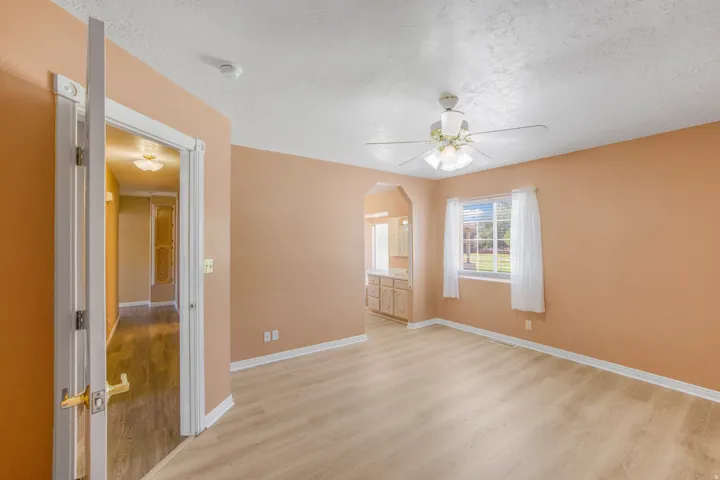 Wood-finish flooring, ceiling fan with integrated lighting, a window providing natural illumination, and an arched doorway leading to an additional space