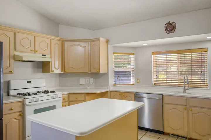 Kitchen featuring wood-finish cabinetry, white countertops, a central island, stainless steel dishwasher, and recessed lighting