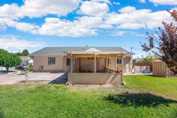 Expansive green lawn, stucco exterior, covered patio, gravel driveway, and a shingled roof