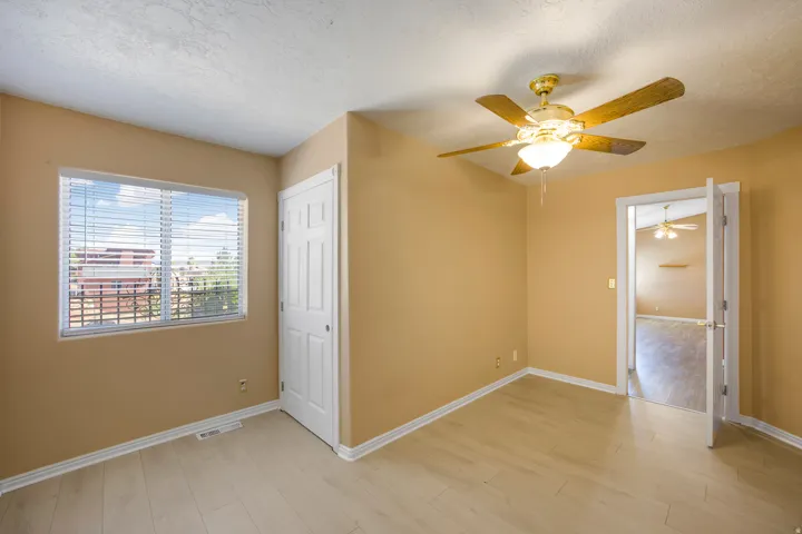 Room featuring a large window with blinds, a ceiling fan with integrated lighting, wood-finish flooring, and a white paneled door