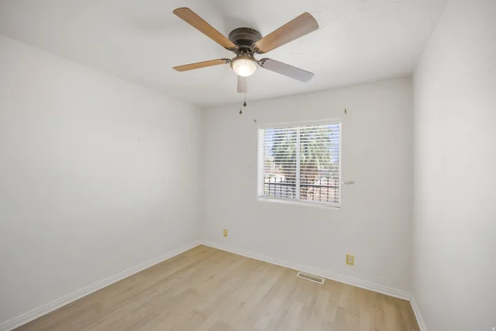 Wood-finish flooring, ceiling fan with integrated lighting, and a window with blinds