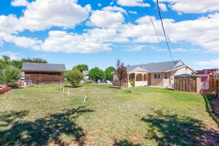 Spacious backyard featuring a covered patio, a detached shed, a storage shed, and a wooden fence