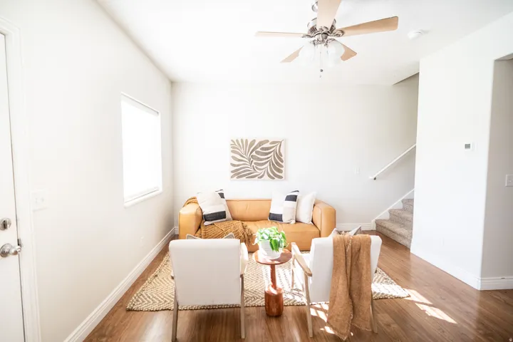 Open concept living space featuring wood-finish flooring, a ceiling fan with integrated lighting, and a window with a roller shade