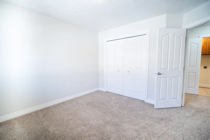 Neutral-toned carpeting, white walls, and a built-in closet with bi-fold doors