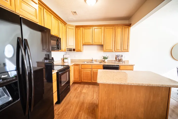 Kitchen featuring wood-finish flooring, wood cabinetry, stone-finish countertops, and black appliances
