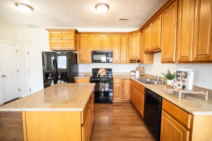 Kitchen featuring wood-finish flooring, wood cabinetry, granite countertops, a kitchen island, and black appliances