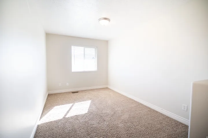 Neutral wall paint with textured carpeting, a window with blinds, and a flush-mount ceiling light