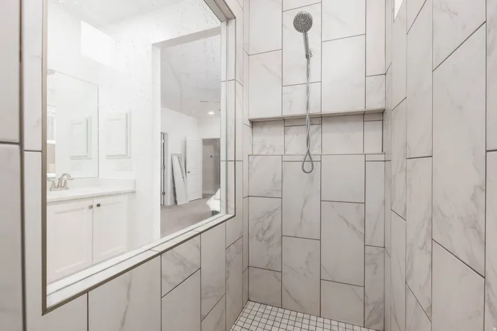 Spa-inspired primary bathroom featuring a walk-in shower with marble-look tile surround, frameless glass enclosure, and rainfall showerhead