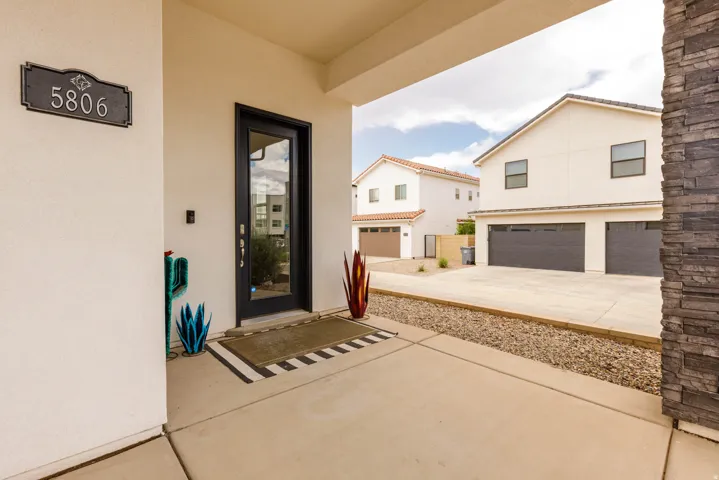Welcoming covered entry featuring a black-framed glass door with sidelights, stamped concrete flooring, and decorative potted plants