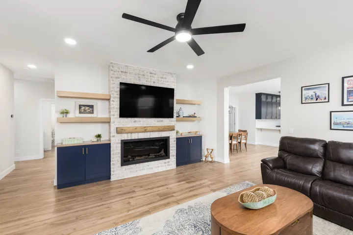 Living area featuring wood-finish flooring, a white brick fireplace, built-in cabinetry, and open shelving