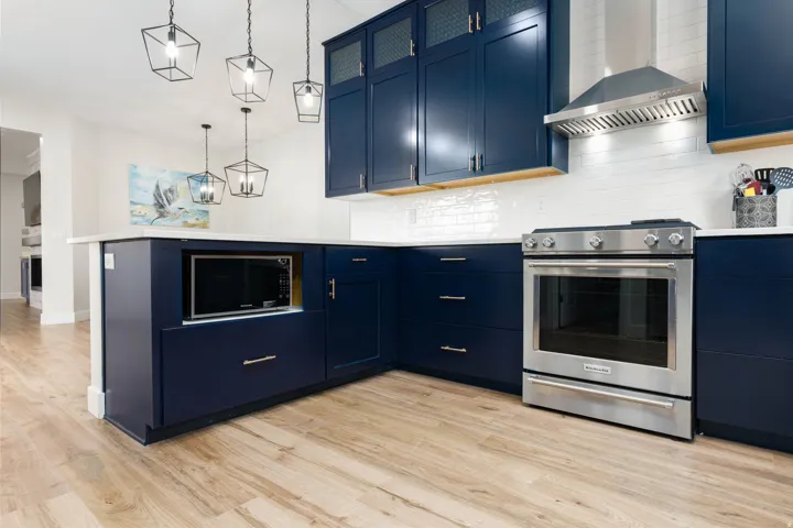 Navy cabinetry, stainless steel range, built-in microwave, white subway tile backsplash, and light wood-finish flooring