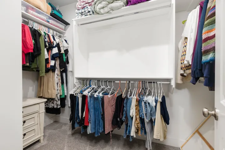 Built-in shelving, multiple hanging rods, and light-colored carpeting