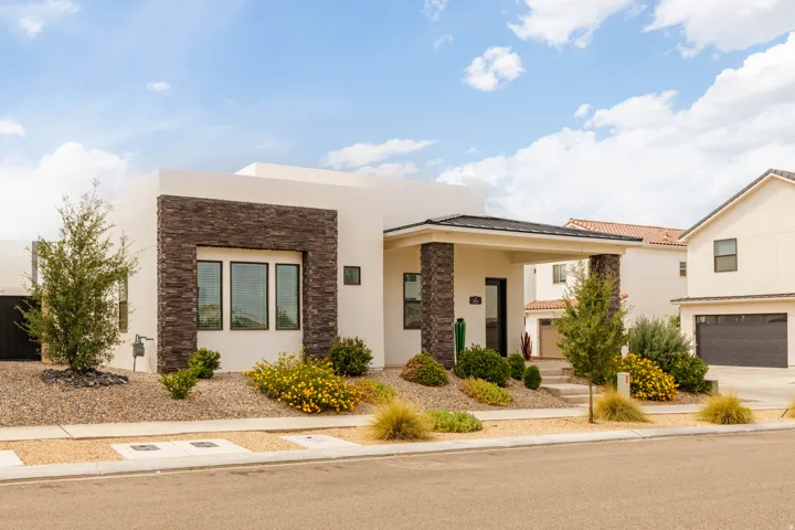 Modern architectural home featuring a striking stone-accented facade, expansive multi-pane windows, drought-resistant landscaping with ornamental grasses, a two-car garage, and clean contemporary lines throughout the exterior design