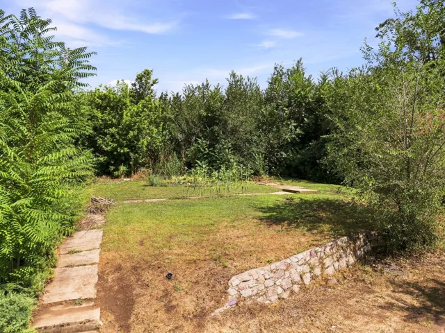 Expansive green space featuring a stone retaining wall, concrete stepping stones, and mature perimeter foliage