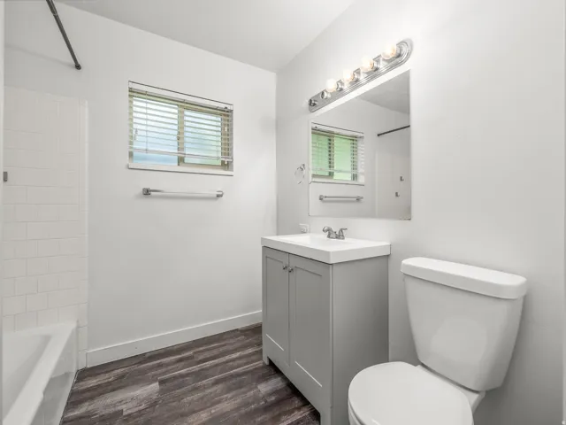 Bathroom featuring a gray vanity with an integrated sink, chrome fixtures, wood-finish flooring, a window with blinds, and white subway tile in the shower area