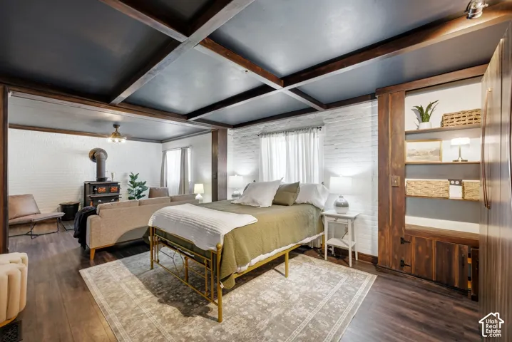 Exposed wood beam ceiling details, wood-finish flooring, white painted brick accent wall, built-in wooden shelving, and a prominent wood-burning stove