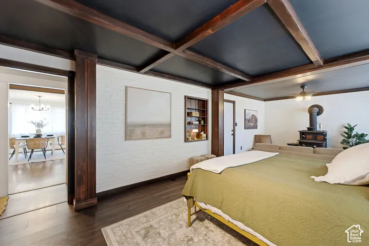 Dark wood-finish coffered ceiling, white painted brick walls, dark wood-finish flooring, wood-burning stove, and built-in shelving unit