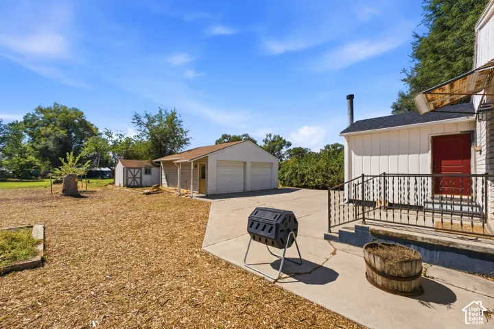 Detached two-car garage, separate storage shed, concrete patio, and exterior stairs with wrought iron railing