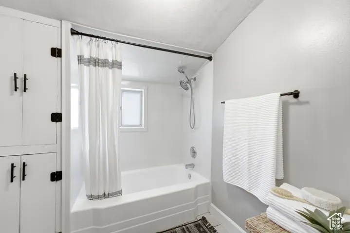 Built-in storage cabinetry with matte black hardware, white bathtub with a wall-mounted showerhead, and a mounted towel bar