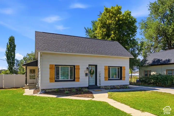 Gable roofline, light-colored siding, black window trim, decorative wood shutters, and paved walkway
