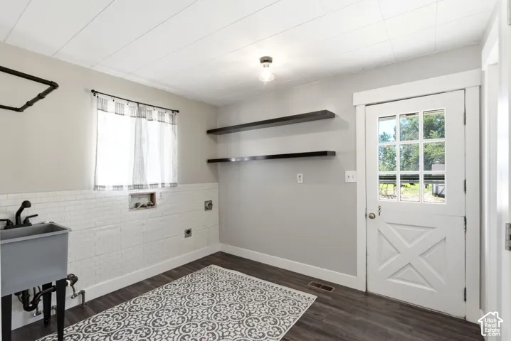 Utility sink with wall-mounted faucet, wood-finish flooring, white subway tile wainscoting, and a panel-style door with glass inserts