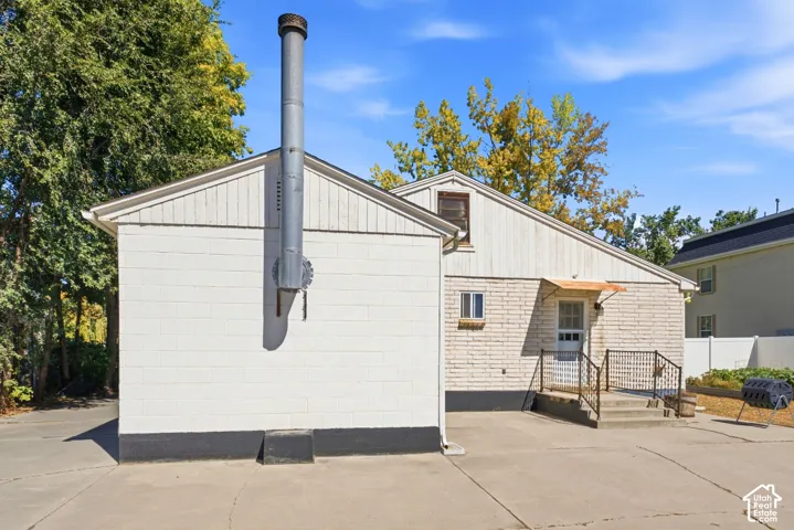 Exterior featuring white painted brick, white siding, a metal chimney, and a concrete patio
