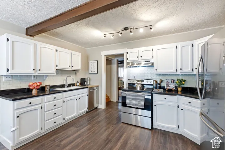 White cabinetry with black hardware, dark countertops, wood-finish flooring, a subway tile backsplash, and stainless steel appliances