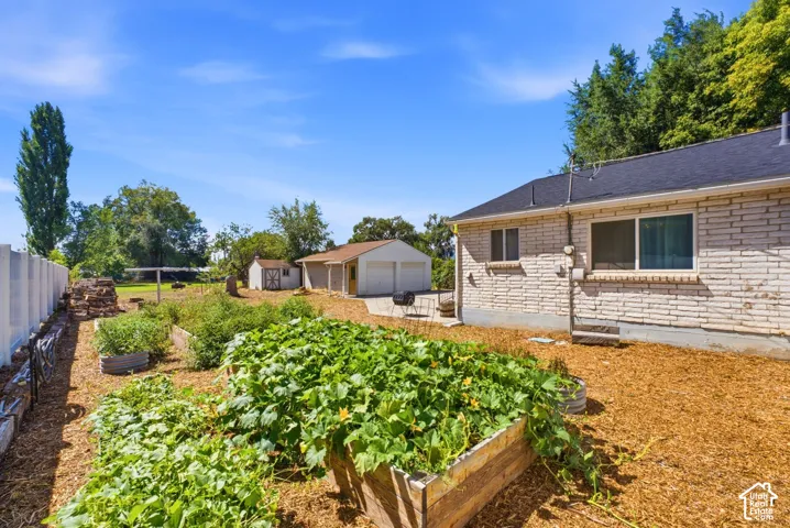 Raised garden beds, detached garage, white picket fence, additional storage shed, and light-colored brick exterior
