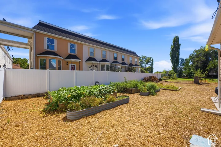 Expansive outdoor space featuring raised garden beds, wood chip ground cover, and a white privacy fence
