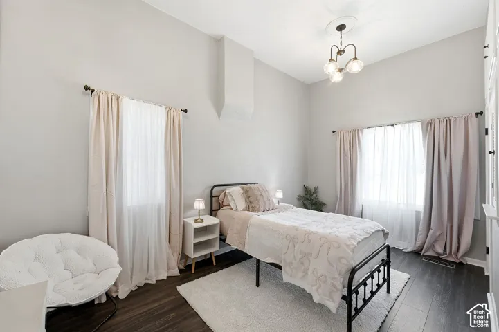 Serene bedroom retreat featuring abundant natural light from dual window banks with layered drapery, dark wood-finish flooring, and a metal-frame bed