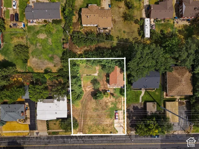 Aerial view of a substantial lot featuring mature landscaping, established trees throughout the grounds, and a brick residence with multiple outbuildings