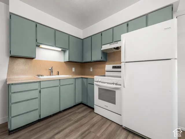 Efficient galley kitchen featuring sage-toned cabinetry with ample storage, wood-finish flooring, and stainless steel appliances including double wall ovens and a refrigerator