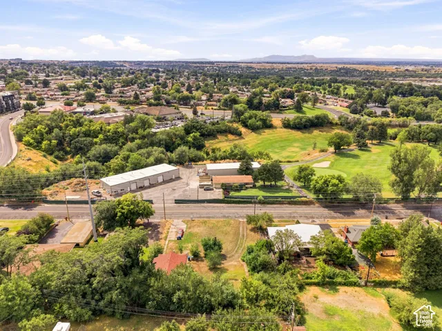 Aerial view showcasing a substantial agricultural or equestrian property with a modern metal-frame barn structure, extensive manicured grounds with mature tree coverage, established pastureland, and direct highway frontage