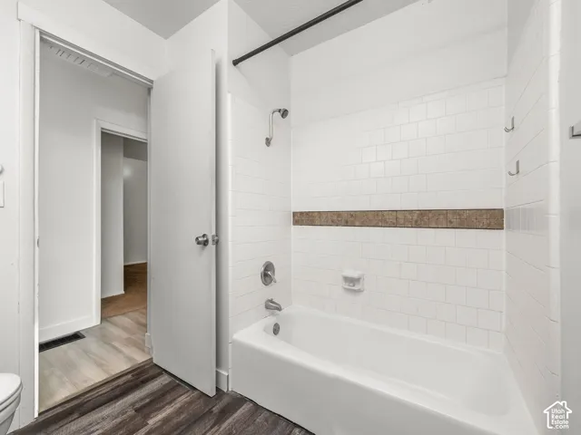 White subway tile shower surround with a decorative accent band, built-in bathtub, and dark wood-finish flooring