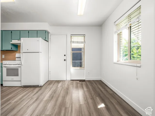Bright kitchen featuring white appliances, wood-finish flooring throughout, and ample natural light from multiple windows