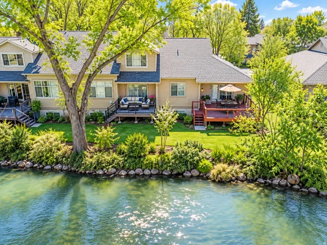 Waterfront property featuring a private deck, stone retaining wall, and verdant landscaping