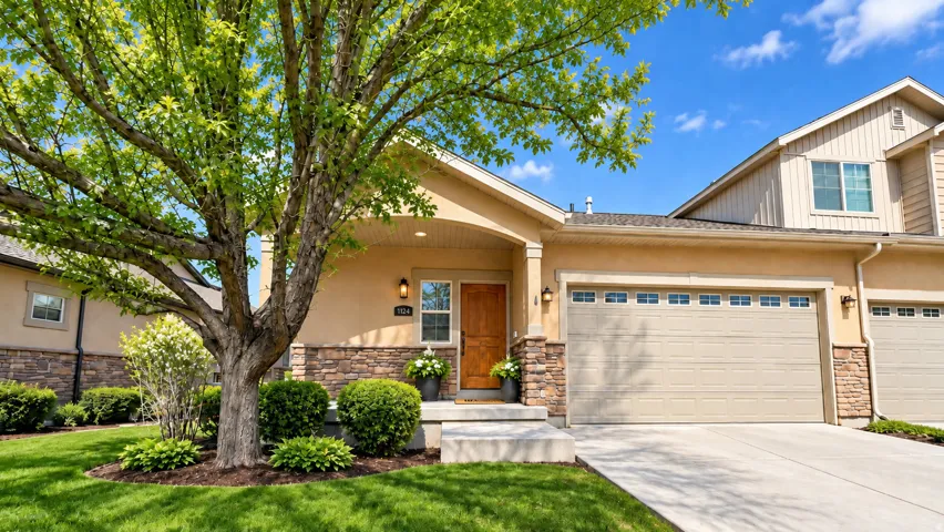 Stucco exterior with stone accenting, prominent front-facing garage with window inserts, covered entryway, and mature tree with surrounding landscaping