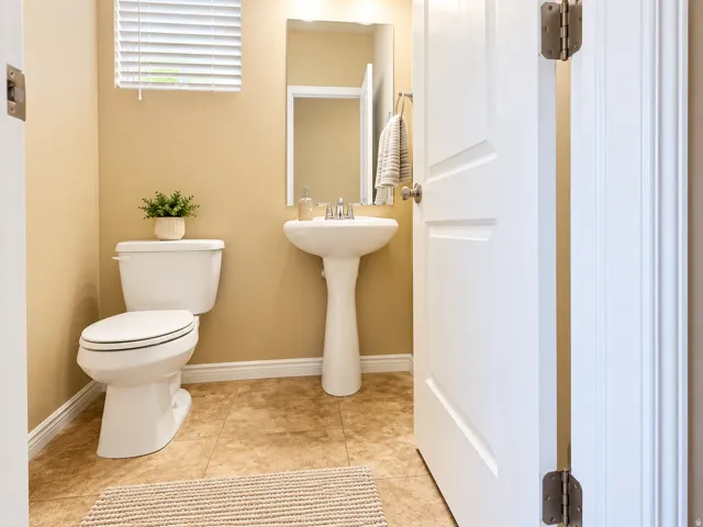 Pedestal sink, white toilet, wall-mounted mirror, and tiled flooring