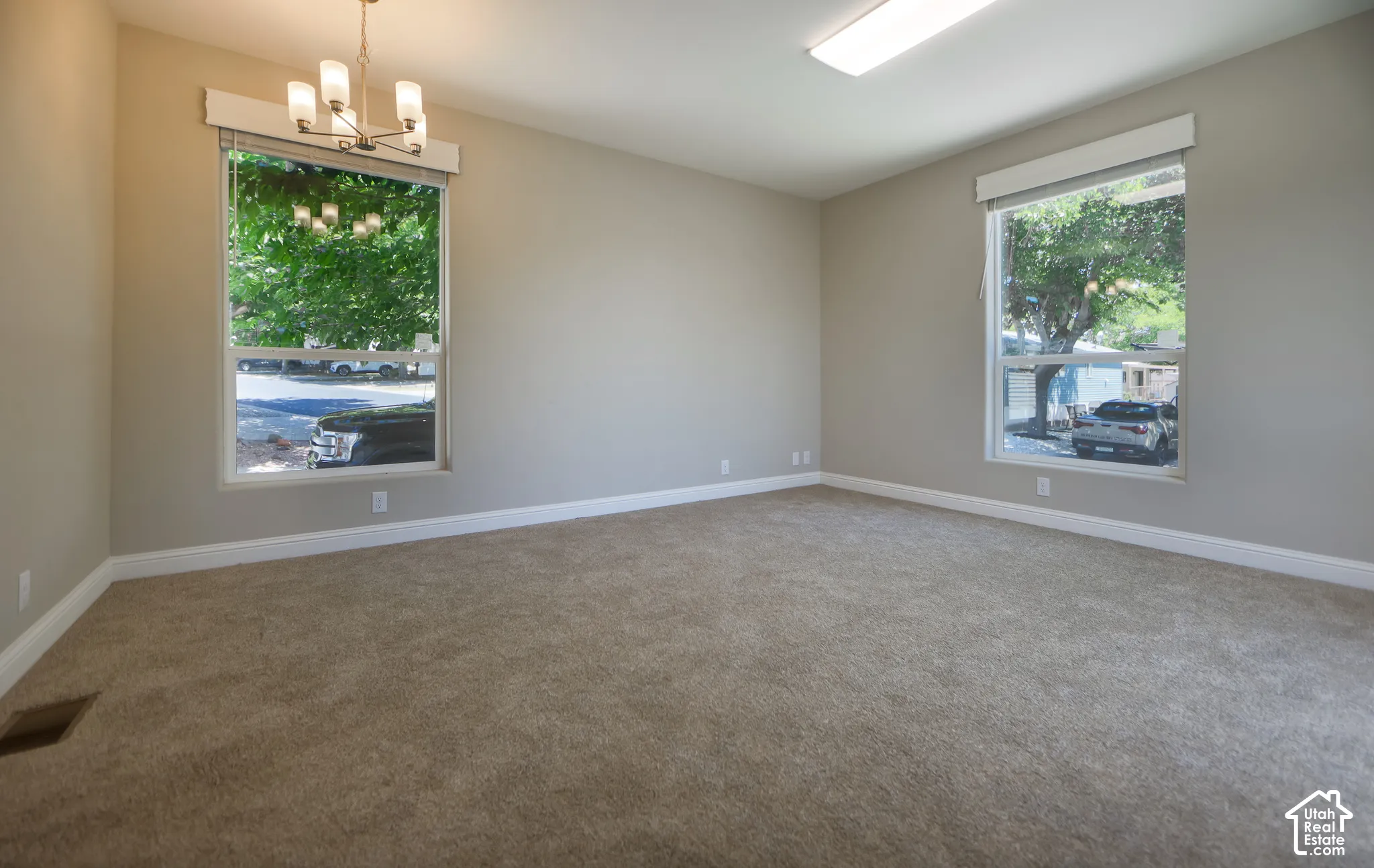Carpet flooring, neutral painted walls, two large windows, a single flush-mount light fixture, and a single chandelier