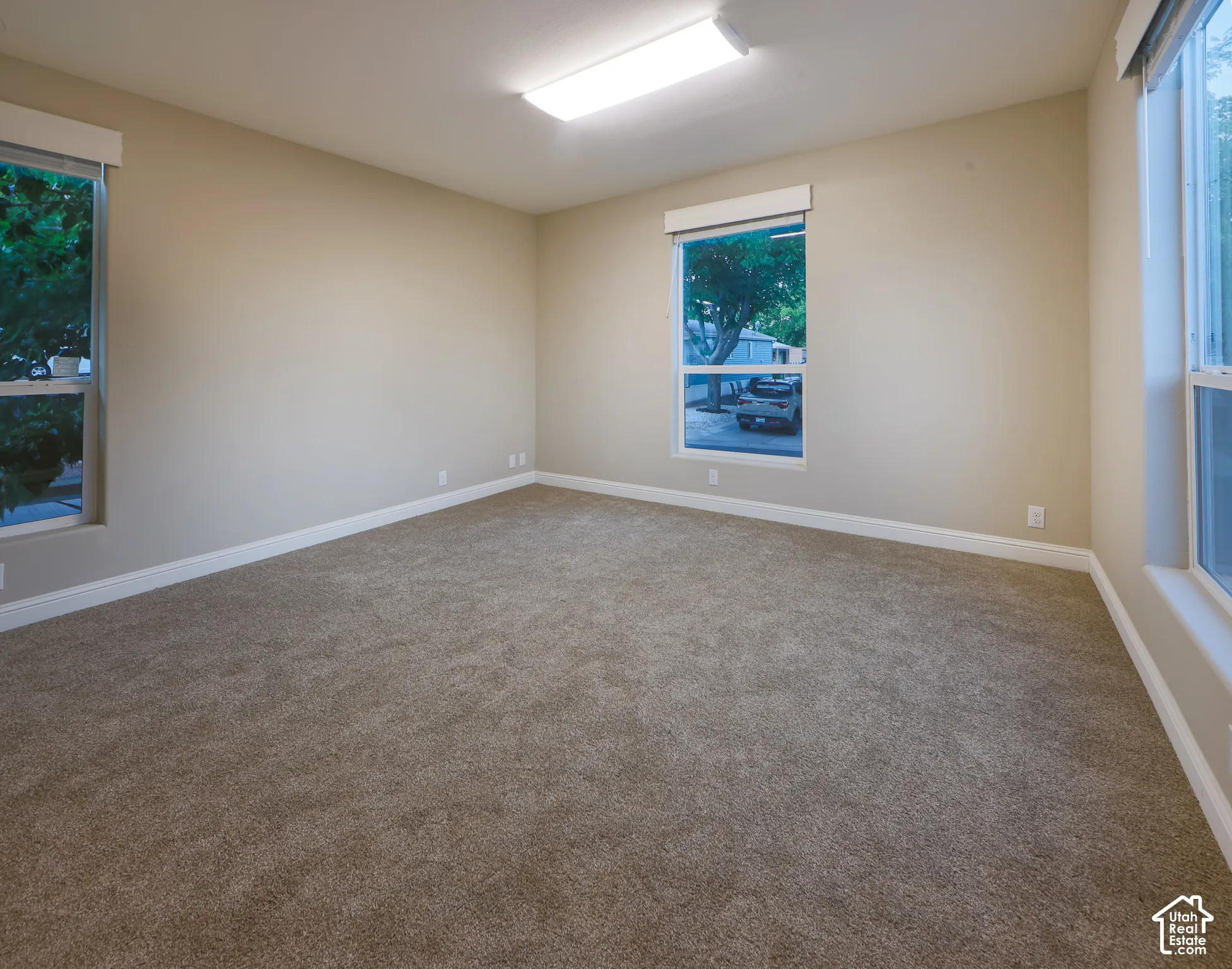 Neutral wall color, wall-to-wall carpeting, multiple windows, and a flush mount ceiling light