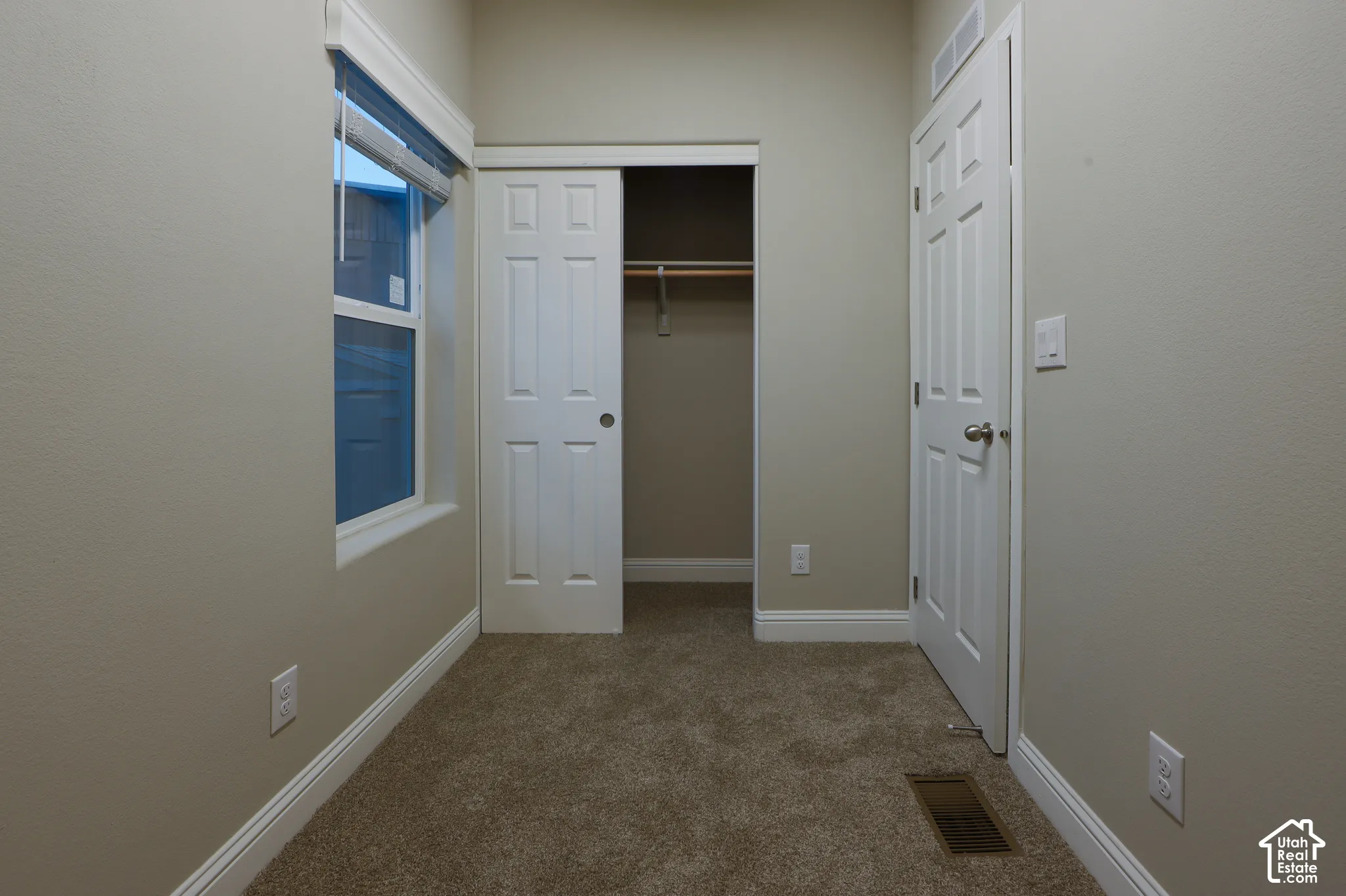 Carpeted room with a window featuring blinds, a closet with sliding doors, and a paneled door