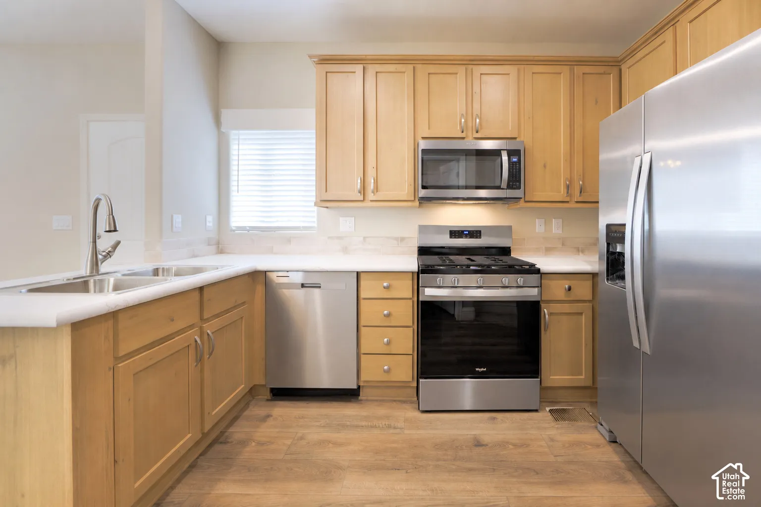 Kitchen featuring wood-finish cabinetry, stainless steel appliances, a double basin sink, and wood-finish flooring