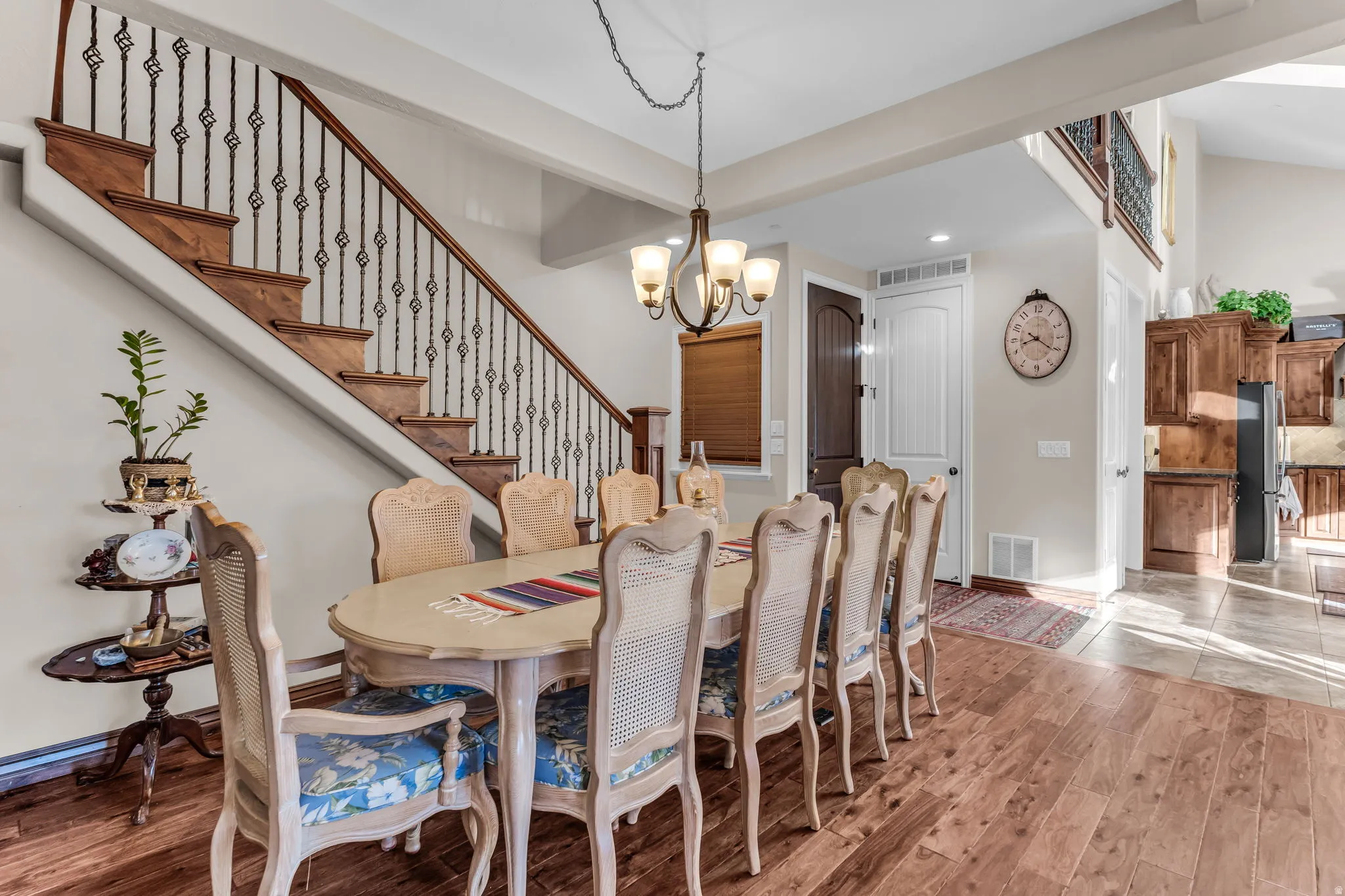 Hardwood flooring, wood staircase with ornate iron balusters, vaulted ceiling, and a multi-light chandelier