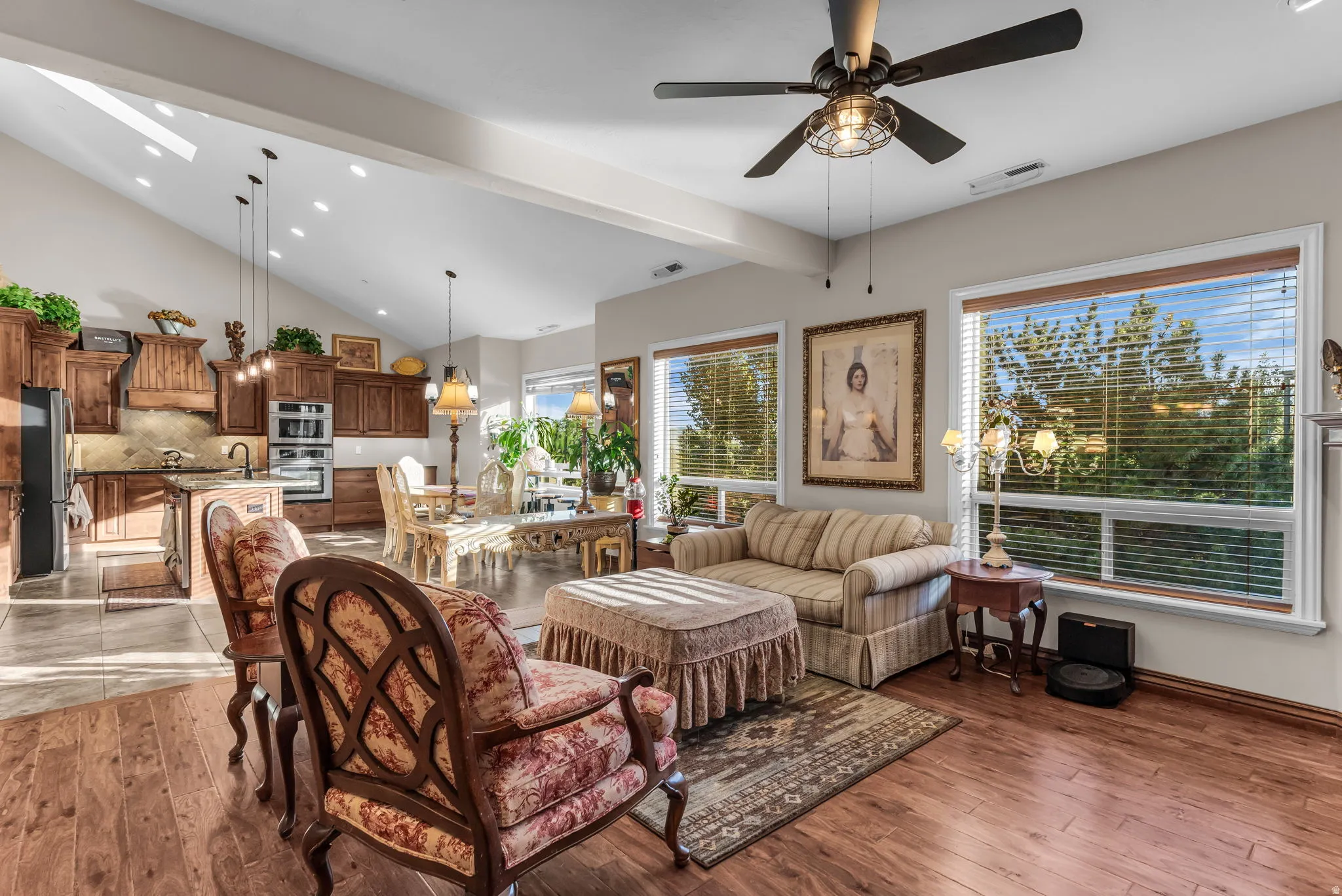 Vaulted ceiling with skylights, wood-finish flooring, built-in kitchen cabinetry, kitchen island, and ceiling fan