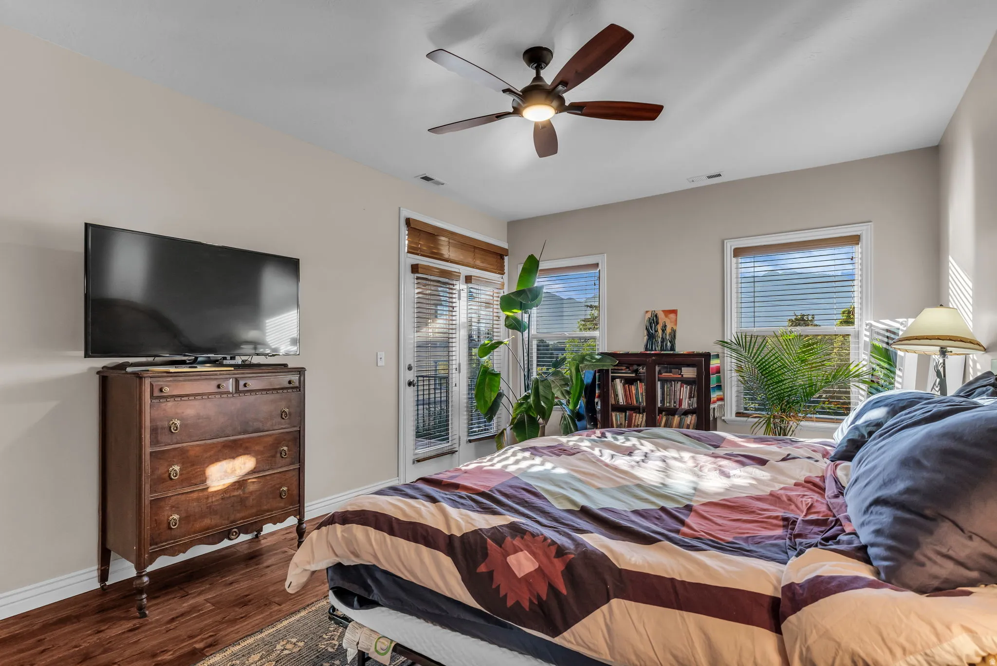 Warm wood-finish flooring, a ceiling fan with integrated lighting, and multiple windows with blinds